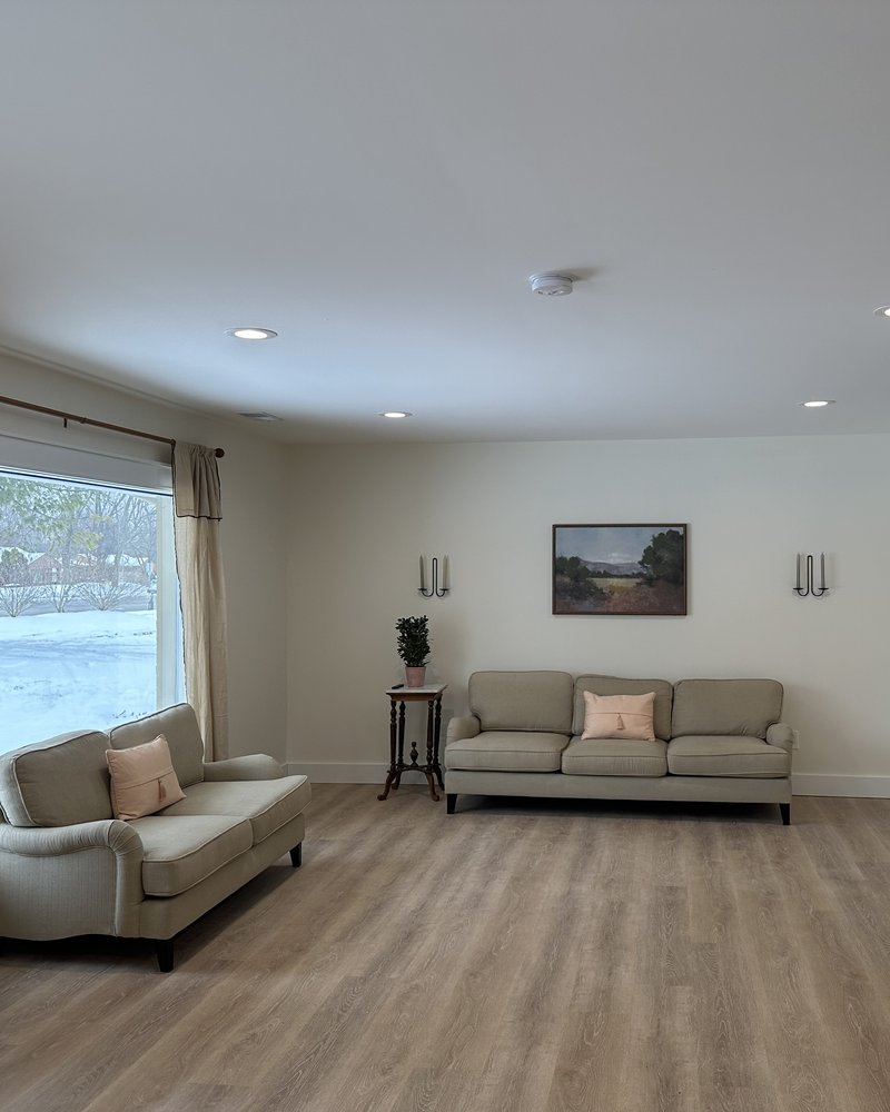 Bright resident living room with beige sofas, a large window, and warm recessed lighting